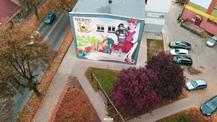 Zdjęcie przedstawiające widok z drona na skwer im. Bartosza Paprockiego. W tle widoczna Miejska Biblioteka Publiczna oraz okolicznościowy mural wykonany na 700. Rocznicę lokacji Miasta Sierpca