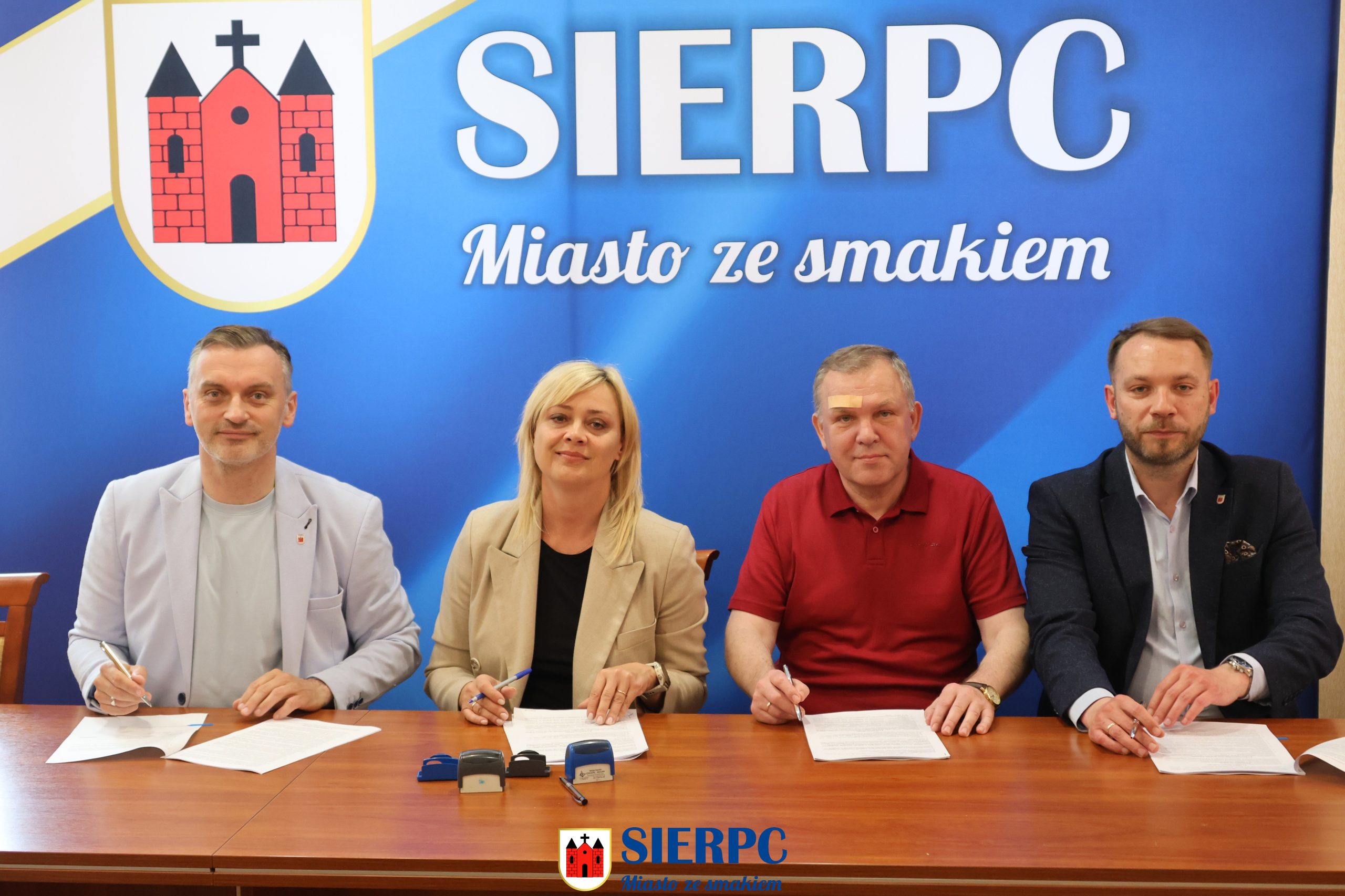 Na zdjęciu widoczne 4 osoby, 3 mężczyzn i 1 kobieta. W tle ścianka reklamowa.